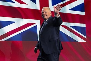 A person in a suit waving, with a large British flag in the background.